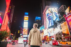 moving to New York in 2020 will give you a chance to experience Time Square like the blond guy in the beige hoody standing in the street.