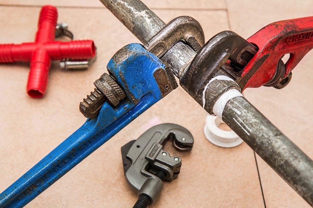 A person who is using a wrench to fix a pipe and is about to realize the downsides of DIY plumbing work.