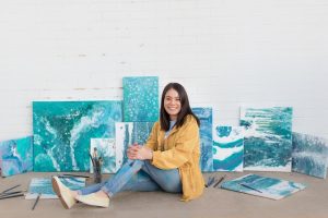 There is a woman sitting on the floor, and there are some paintings behind her. 