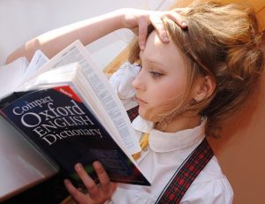 A girl holding a dictionary, trying to figure out what certain words mean.