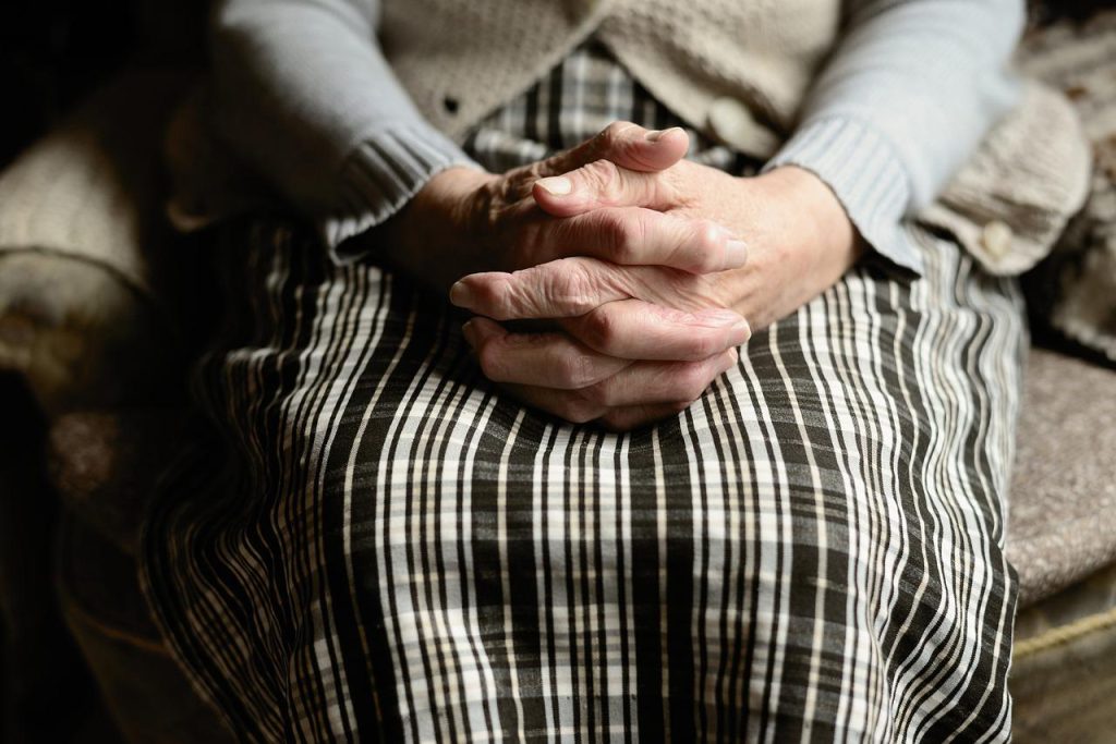 An elderly woman holding hands in her lap.